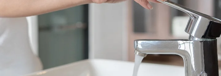 Hand dreht einen Wasserhahn auf.